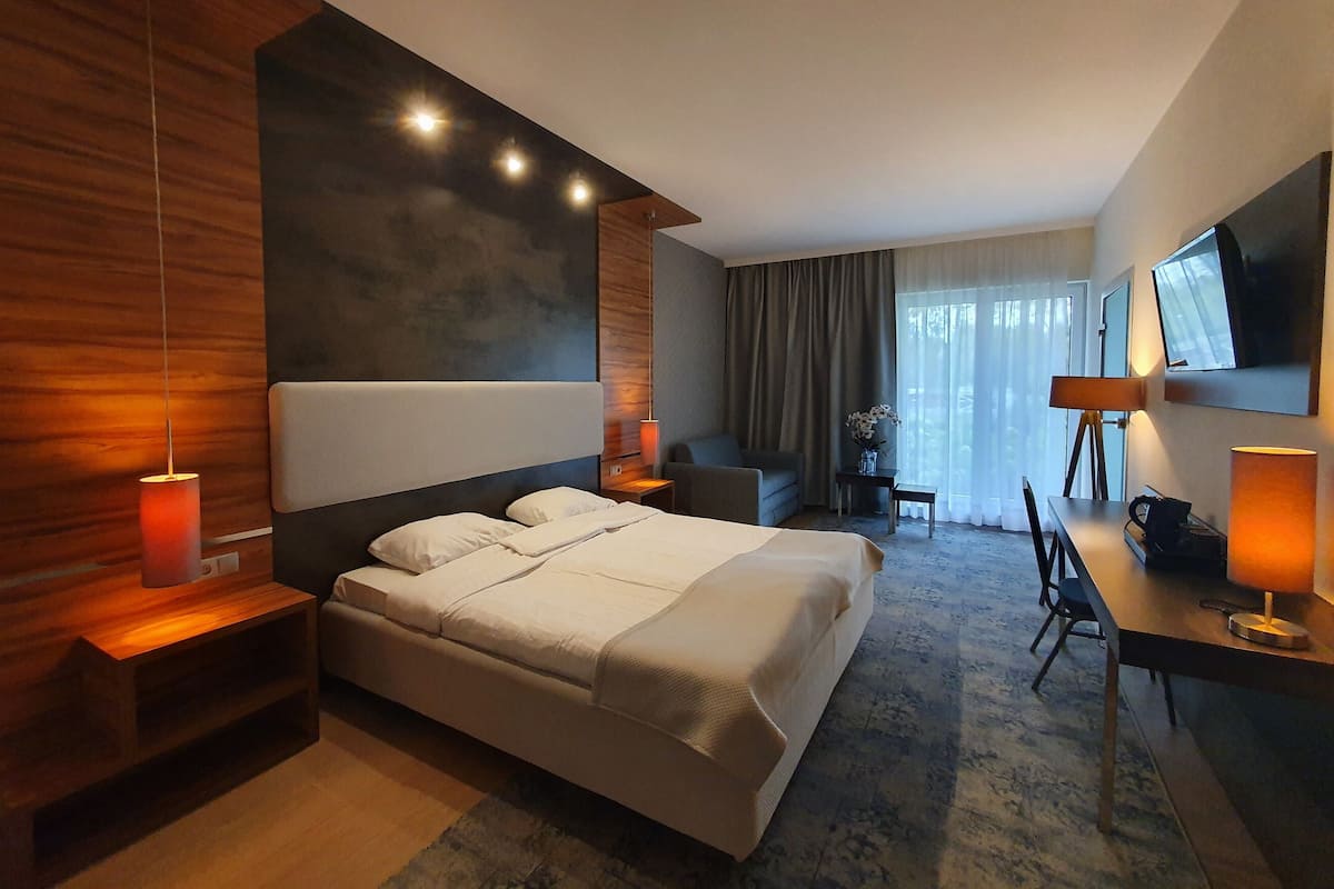A modern hotel room with a large bed, a desk, a chair, and a TV on the wall.