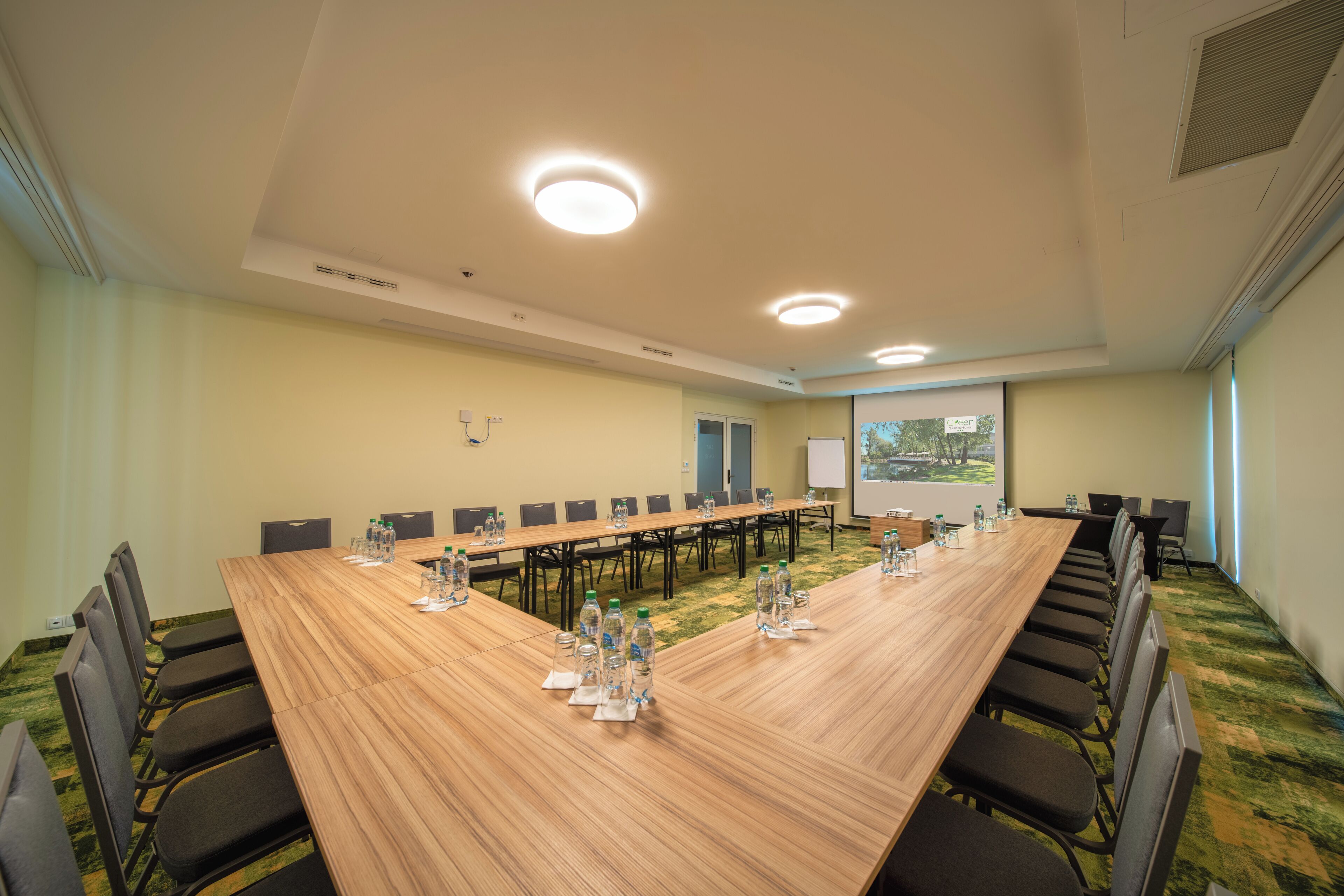 Una sala de conferencias con una larga mesa, sillas, botellas de agua y una pantalla de proyector.