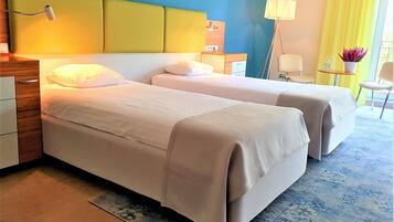 Een hotelkamer met twee bedden, een nachtkastje van hout, een bureau, een stoel, een klein tafeltje met een lamp en een kamerplant.