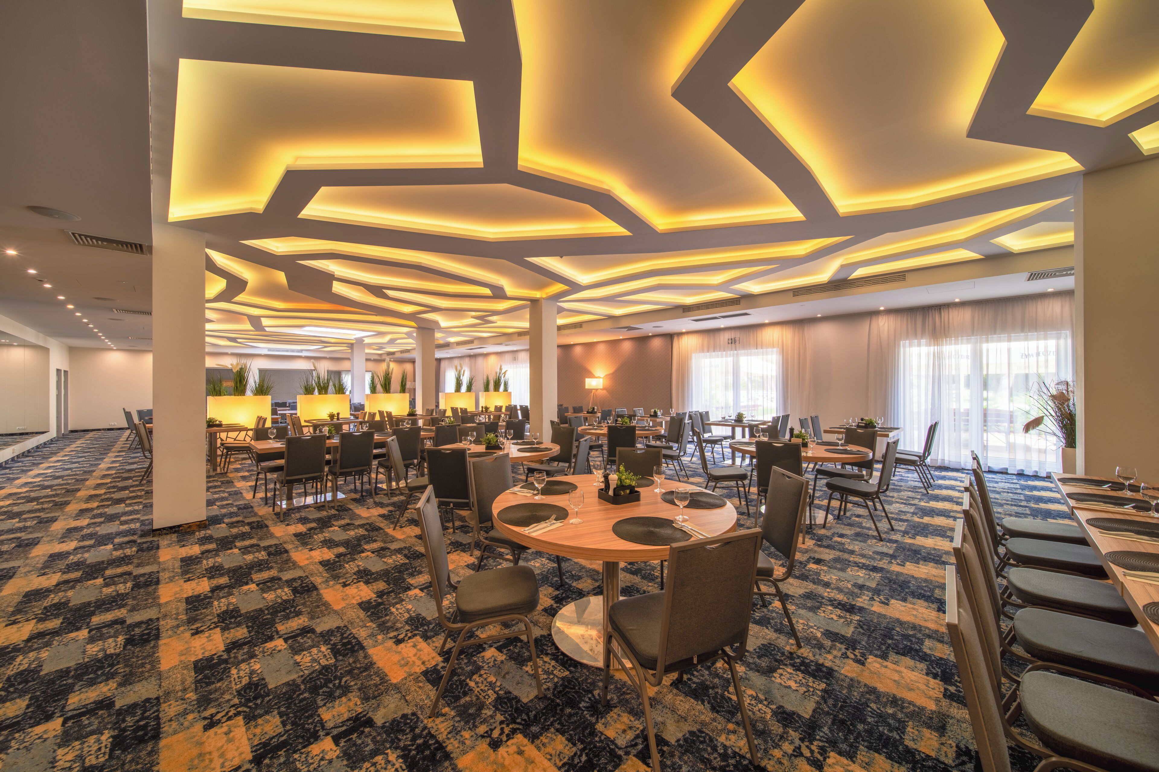 A hotel dining area with round tables, chairs, and a patterned carpet.