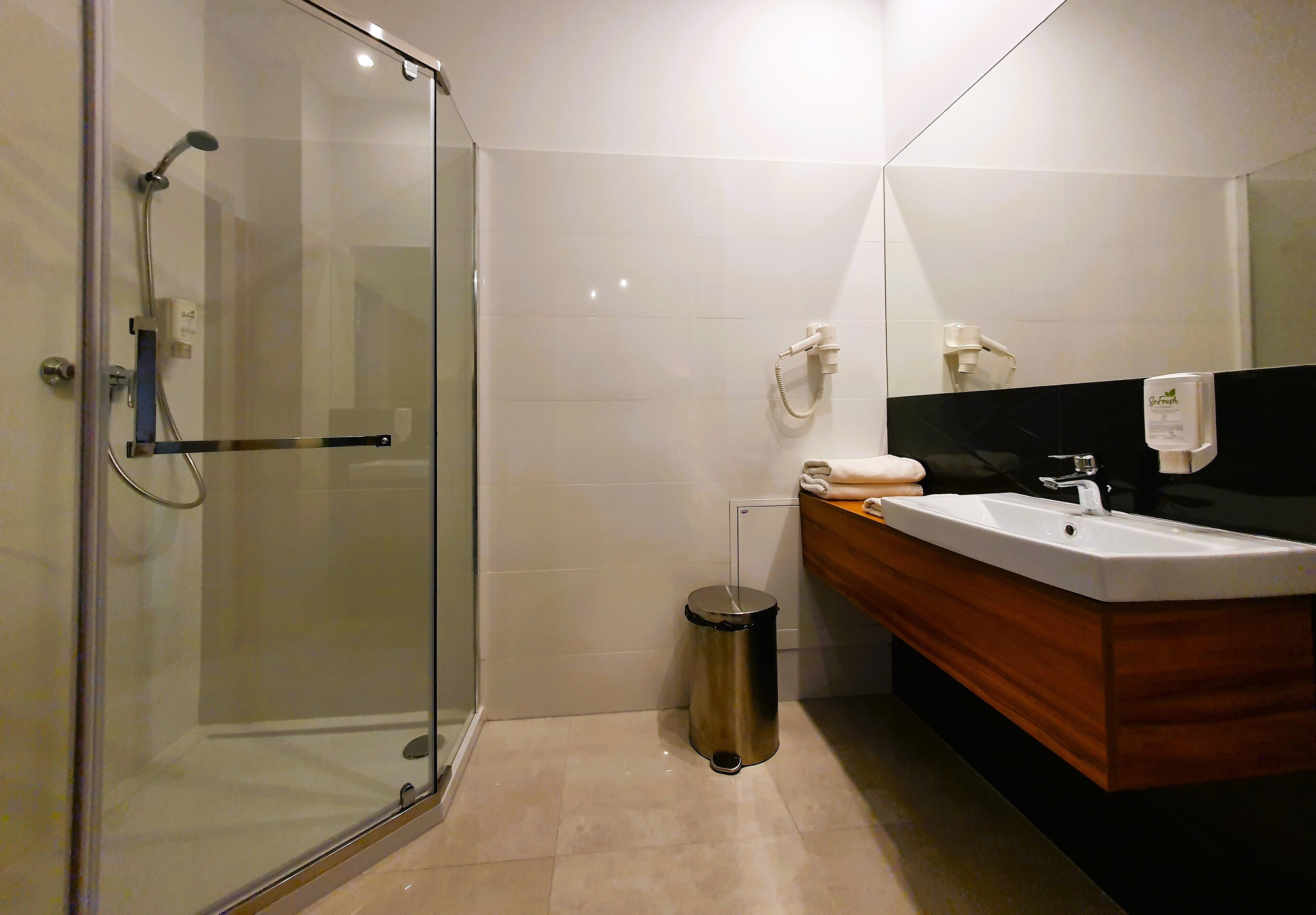 Un baño moderno con ducha envuelta en vidrio, tocador de madera con lavamanos y espejo.