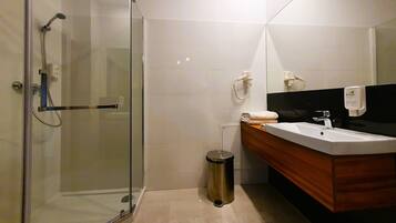 Un baño moderno con ducha envuelta en vidrio, tocador de madera con lavamanos y espejo.