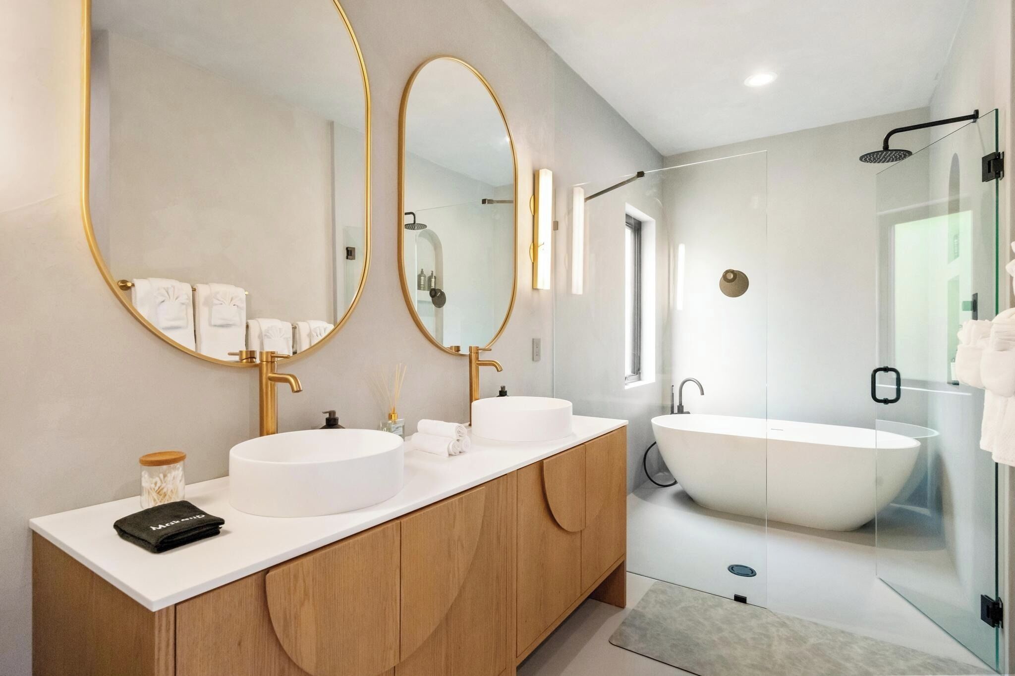 A modern bathroom with two round mirrors, a freestanding bathtub, and a glass-enclosed shower area.