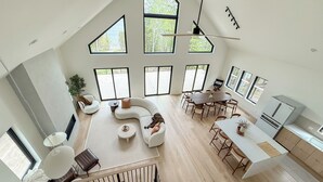 Un vaste espace de vie comprenant un canapé blanc incurvé, une table à manger avec des chaises et un coin cuisine équipé d’un réfrigérateur.