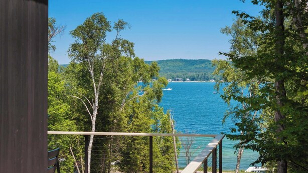 Une terrasse en bois donnant sur un lac où l’on peut voir des bateaux, le tout entouré d’arbres.
