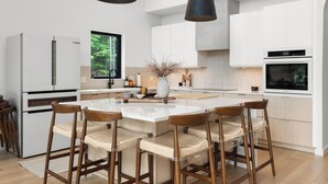 Une cuisine moderne dotée d’un îlot central, de tabourets de bar, de luminaires suspendus et de meubles blancs.