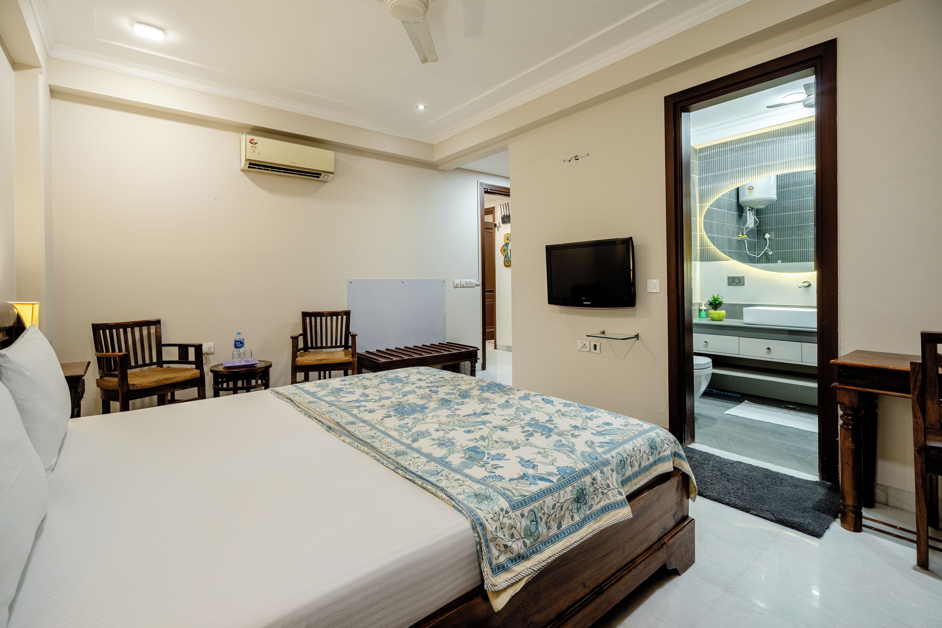 A hotel room with a bed, a desk, a chair, a TV, and a bathroom visible through an open door.