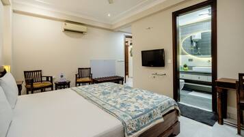 A hotel room with a bed, a desk, a chair, a TV, and a bathroom visible through an open door.