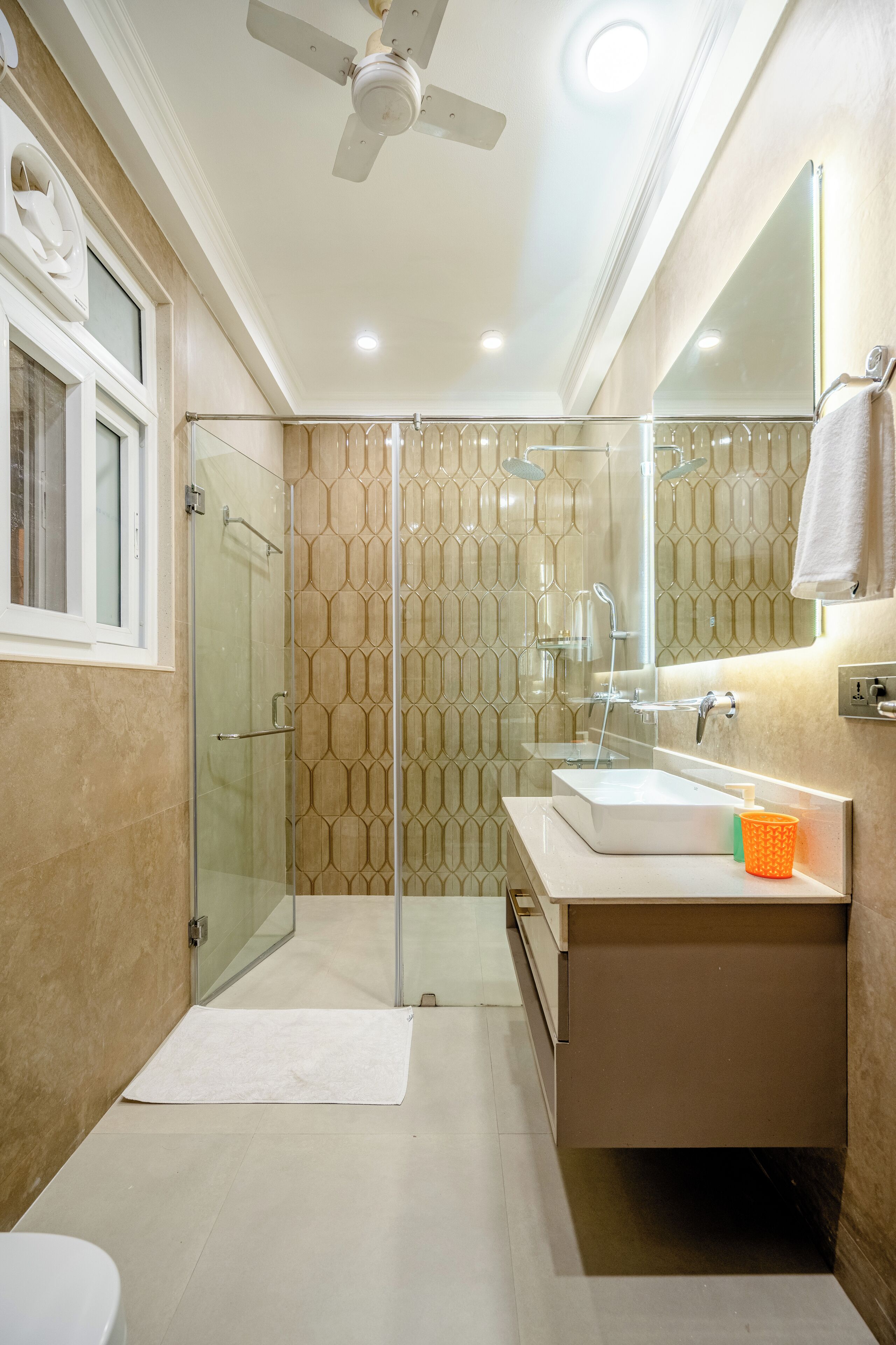 A modern bathroom with a glass shower enclosure, a vanity with a mirror, and a ceiling fan.