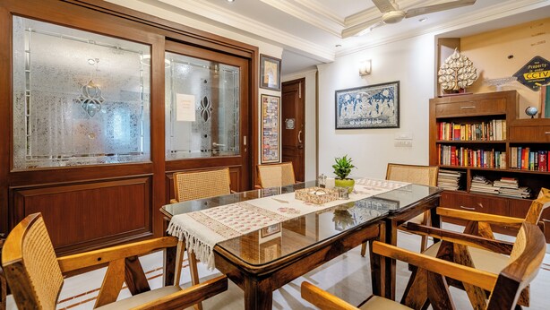 Un comedor con una mesa de vidrio, sillas de madera y una estantería.