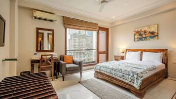 A bedroom with a bed, a chair, a desk, a mirror, and a window with a view.