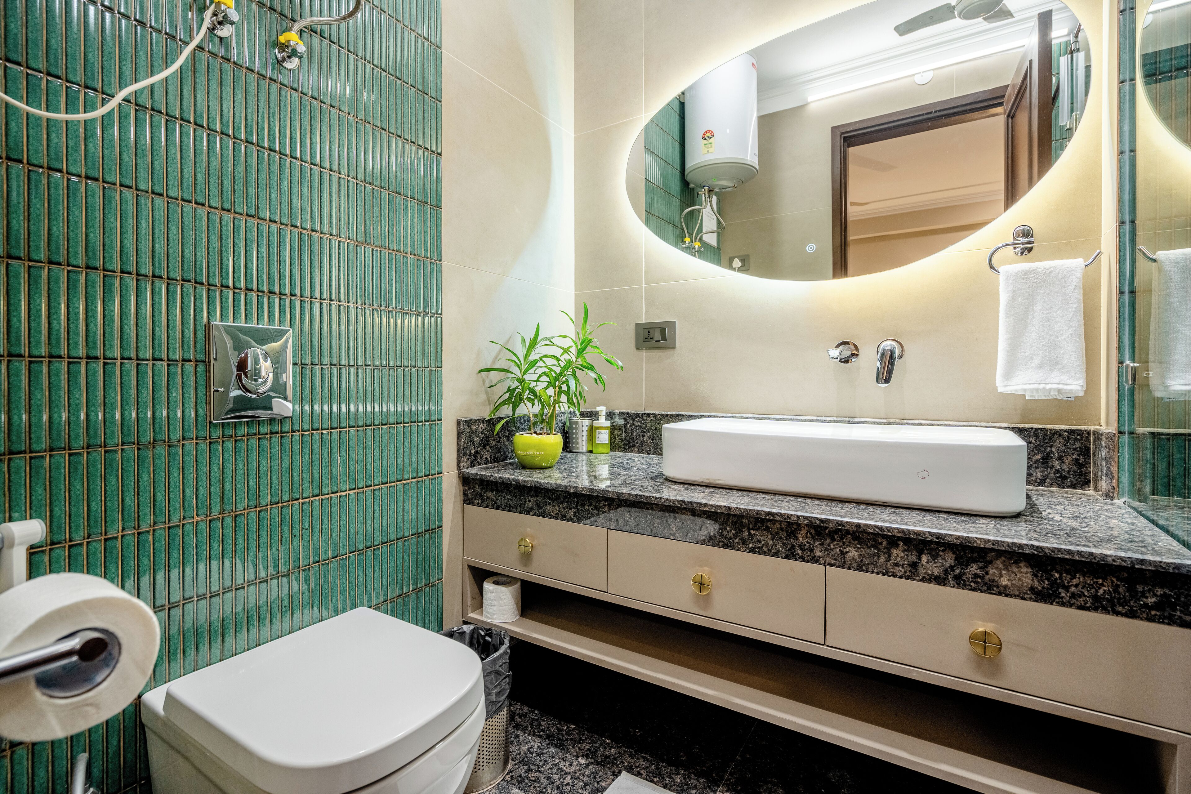 Un baño con pared de azulejos verdes, un lavamanos blanco, un espejo y un inodoro.