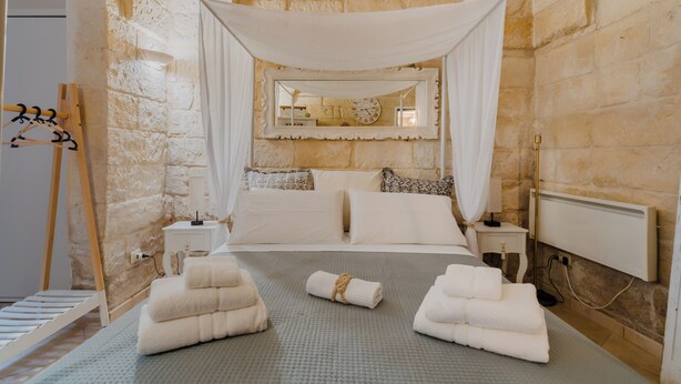 A bedroom with a stone wall, a canopy bed, a bedside table, and a hanging rack. - Suite Corte Volturio by BarbarHouse (Lecce)