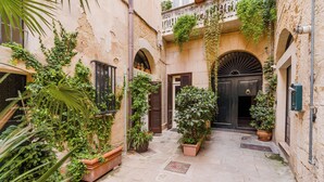 A narrow courtyard with stone flooring, potted plants, and a black door. - Suite Corte Volturio by BarbarHouse (Lecce)