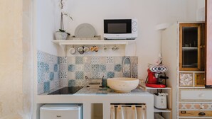 A compact kitchen with a microwave, sink, and small refrigerator. There is a shelf with dishes and a potted plant. - Suite Corte Volturio by BarbarHouse (Lecce)