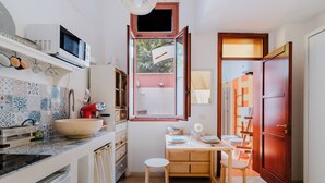 A compact kitchen with a large island, a microwave, and a sink. There is a window with a view of greenery outside. - Suite Corte Volturio by BarbarHouse (Lecce)