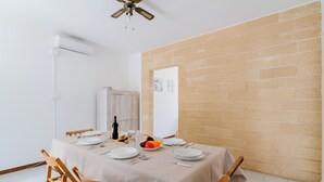 Un comedor con una mesa lista para cuatro personas, un ventilador de techo y una pared de ladrillo.