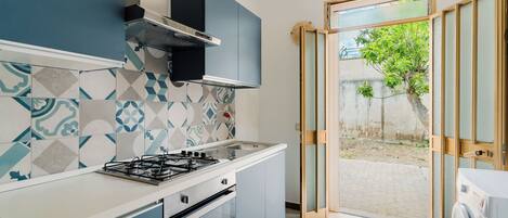 A modern kitchen with a gas stove, oven, and built-in cabinets. There is a sliding glass door leading to a patio area with a tree.