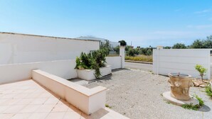 Una terraza en la azotea con un muro blanco, una jardinera con follaje, una fuente de piedra y una entrada protegida por una reja.