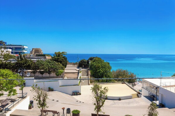 A coastal view with a clear blue sky, a sandy beach area, and a staircase leading down to the beach.