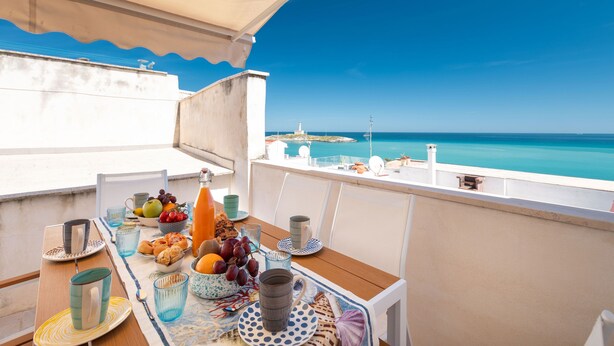 A balcony with a table set for breakfast, overlooking a clear blue sea and a lighthouse. - Villa Helena by BarbarHouse (Vieste)