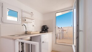 A compact kitchen with a sink, a coffee machine, and a small refrigerator. There is a window above the sink and a door leading to an outdoor balcony. - Villa Helena by BarbarHouse (Vieste)