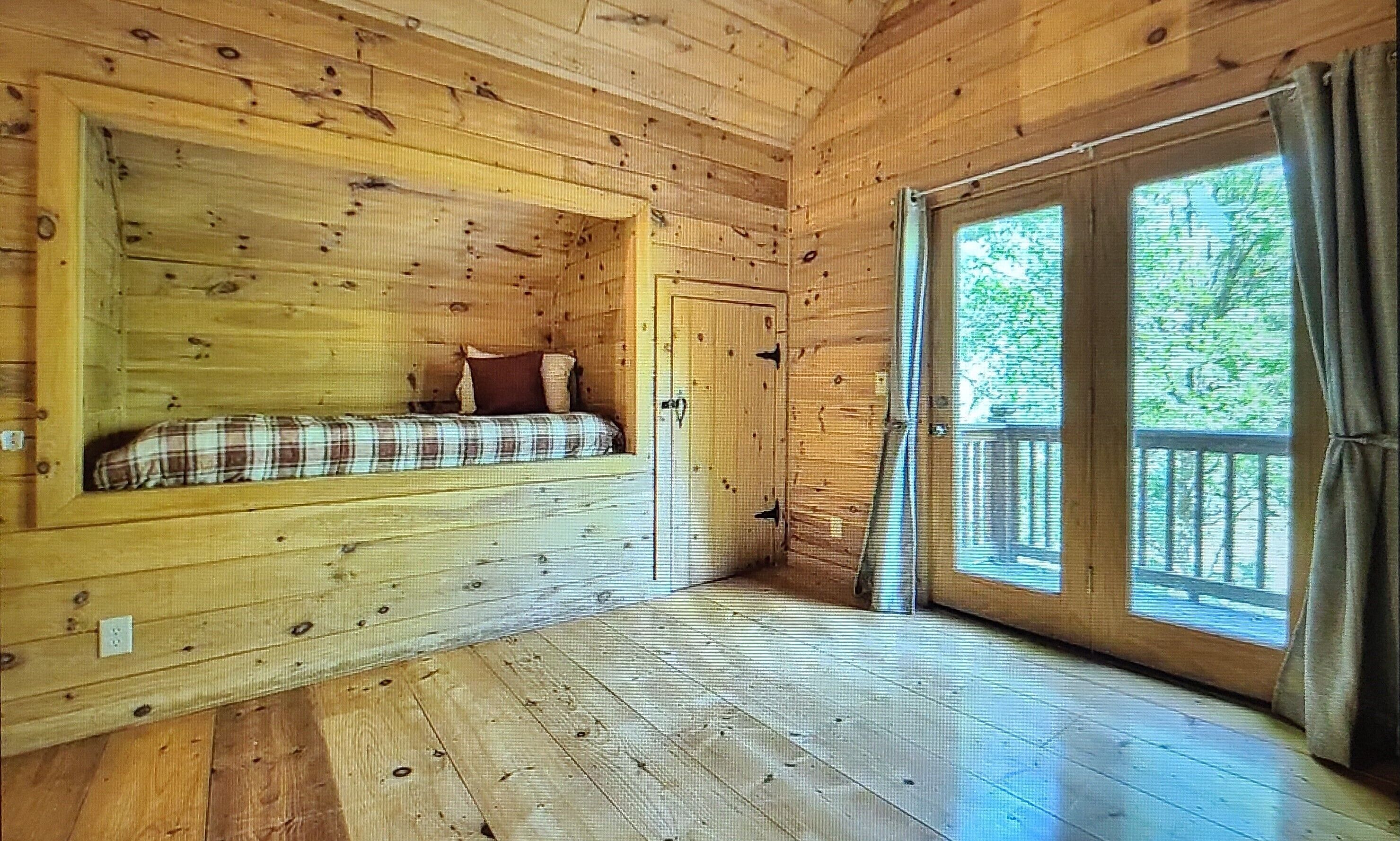 Una cabaña con cama en altillo, ventana con cortinas y suelo de madera.