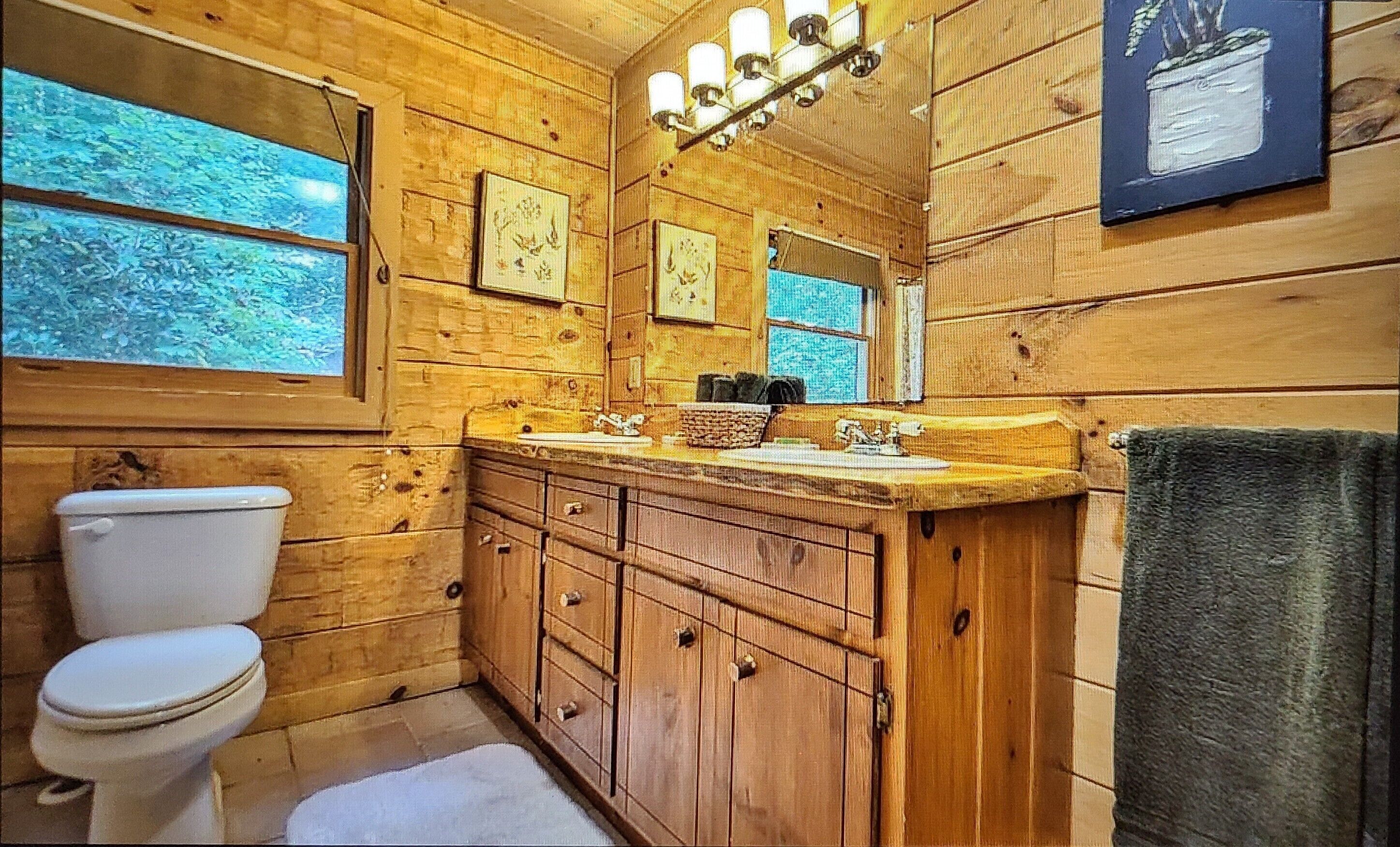 A wooden cabin bathroom with a toilet, wooden cabinets, a sink, and a large mirror.