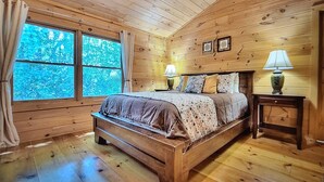 Ein Schlafzimmer in einer Holzhütte mit einem Bett, zwei Nachttischlampen und einem Fenster mit Vorhängen.