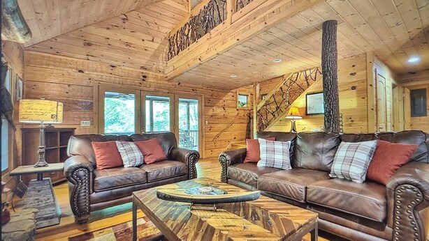Ein gemütliches Interieur im Chalet-Stil mit zwei Ledersofas, einem Holztisch und einer Treppe, die zu einer oberen Ebene führt.
