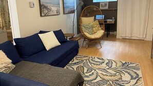A living room with a blue sofa, a rattan chair, a patterned rug, and artwork on the walls. - Large, fully-equipped apartment - private access (ideal for visiting Quebec City) (Lévis)