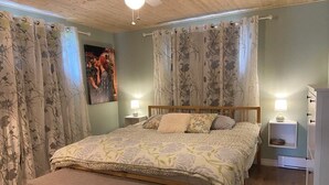 A bedroom with a wooden bed, floral curtains, a bench, and bedside lamps. - Large, fully-equipped apartment - private access (ideal for visiting Quebec City) (Lévis)