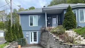 A two-story house with a front porch, a stone retaining wall, and a driveway. - Large, fully-equipped apartment - private access (ideal for visiting Quebec City) (Lévis)
