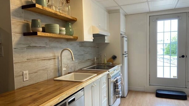 A kitchen with wooden countertops, a sink, a stove, and a refrigerator. There are shelves above the counter holding dishes and glasses. - Large, fully-equipped apartment - private access (ideal for visiting Quebec City) (Lévis)
