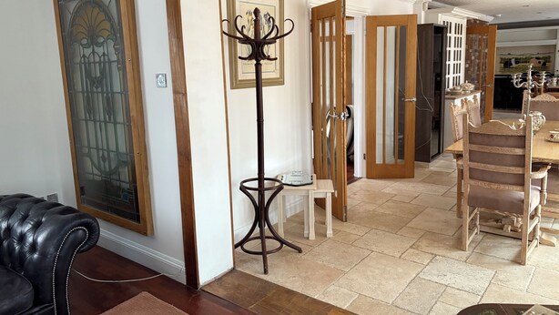 Een ruime woonruimte met een grote zwarte leren bank, een hoge vloerlamp en een eethoek met houten stoelen en een tafel.