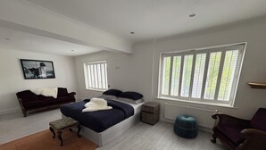 Een slaapkamer met een groot bed, een raam met jaloezieën, een radiator, een kleine tafel en een stoel.