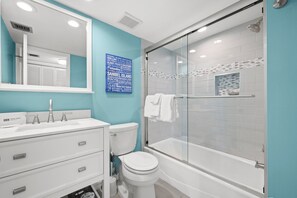 A modern bathroom with a white sink, toilet, and bathtub, a glass shower enclosure, and a blue accent wall.