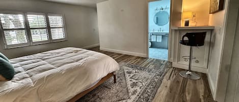 Un dormitorio con cama, alfombra, ventilador de techo y vista a un baño a través de una puerta abierta.
