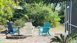 A patio area with three Adirondack chairs, a fire pit, and lush greenery. - Walk to Beach, Dining, Shops, Screen Patio, Game Room, Hobe Sound Zeus Park (Hobe Sound)