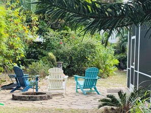 Un patio con tres sillas tipo Adirondack, un pozo de fuego y abundante vegetación.