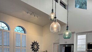 A modern kitchen with white cabinetry, a large island, and stainless steel appliances. There are wicker chairs and a sunburst wall decoration. - Walk to Beach, Dining, Shops, Screen Patio, Game Room, Hobe Sound Zeus Park (Hobe Sound)