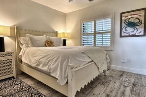 Cama bem arrumada com cabeceira, abajures e uma janela com persianas.