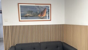 Una sala moderna con un sofá gris oscuro, un cuadro con un paisaje y una pared de listones de madera.