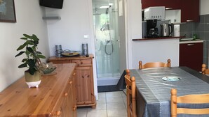 Una cocina compacta con comedor, armarios de madera, microondas integrado y cabina de ducha de vidrio.