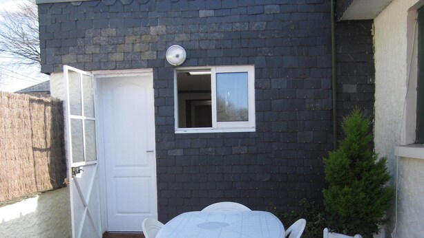 Un patio con una mesa y sillas blancas, una ventana pequeña y una puerta.