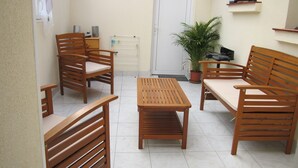Habitación con muebles de madera, incluyendo un sofá, sillas y una mesa. Se observa una planta en maceta y una puerta al fondo.