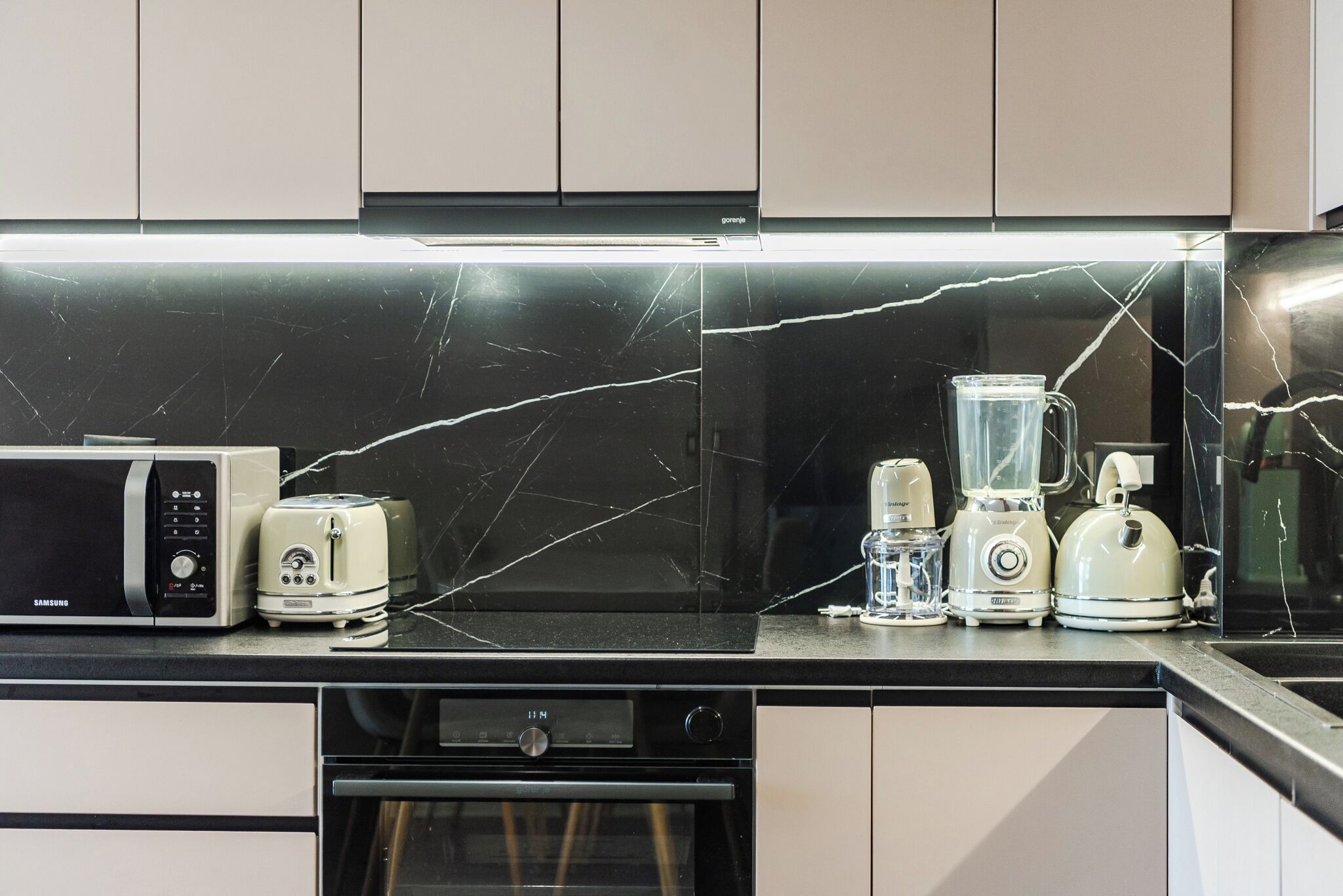 A kitchen with a black marble countertop, a microwave, a toaster, a blender, and a kettle.