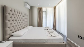 A modern hotel room with a tufted headboard, a large bed with white linens, and a view of the outdoors through sheer curtains.