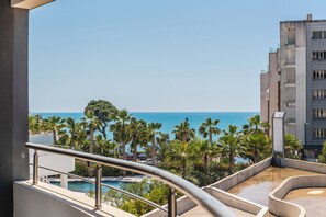 Un balcón con vistas al mar, palmeras y un edificio moderno.