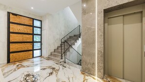 A modern interior with a marble floor, a wooden door with glass panels, a staircase with a metal railing, and a large door.